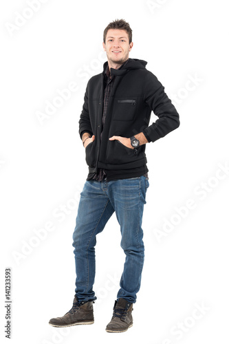 Young casual smiling man in hooded winter jacket with hands in pockets. Full body length portrait over white studio background. © sharplaninac