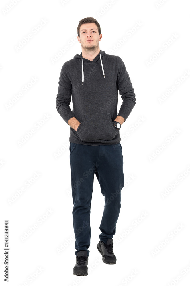 Front view of confident young man in sportswear walking with hands in pockets. Full body length portrait over white studio background. Front view of confident young man in sportswear walking with hands in pockets. Full body length portrait over white studio background.