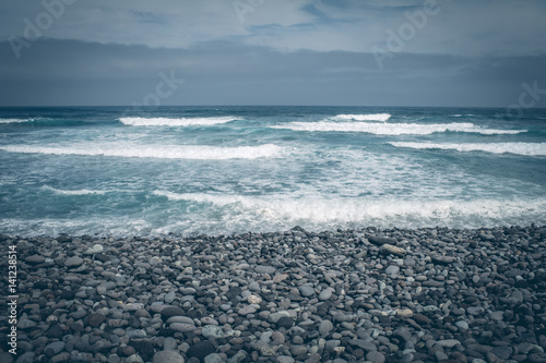 pebble stones by the sea. Silky waves of blue sea from long exposure.