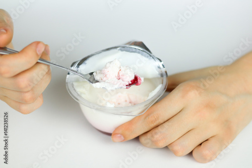 Girl's hand stirred with a spoon of natural yogurt and red jam. Yogurt on the spoon close up. Isolated on white background