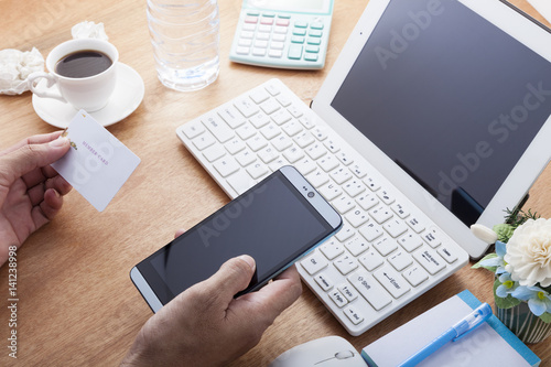 hand use smartphone with hand holding credit card on wood desk at home office, concept online payments shopping .