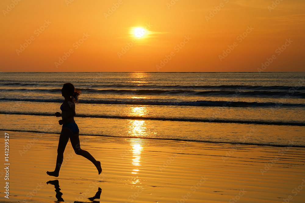 Silhouette of woman jogger running on sunset beach with reflection, fitness and sport concept
