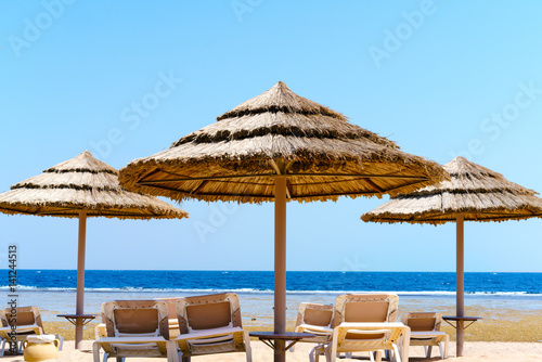 Beach straw umbrellas and sunbeds on the sandy sea shore. A bright sunny day. Clear blue sky.