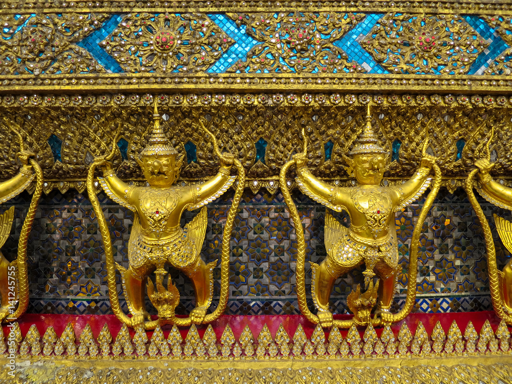 Golden garuda holding naga statue row with ornamental decoration on temple wall