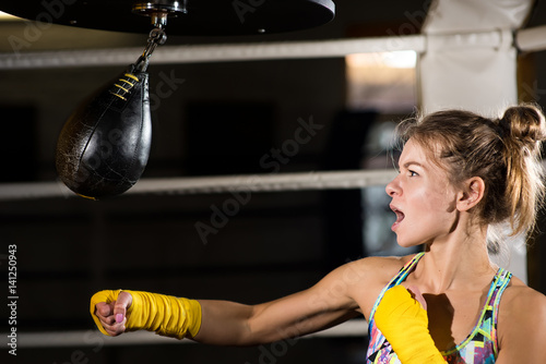 Concentrated woman doing a fitness boxing workout with a punching bag. The girl in the boxing hall emotionally beats the boxing bag photo