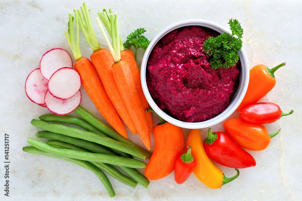 Beet hummus dip with a variety of fresh vegetables, above view on a white marble background
