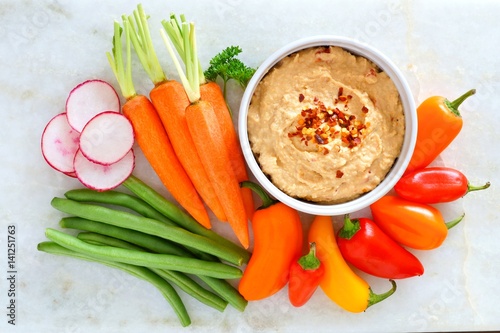 Hummus dip with a variety of fresh vegetables, above view on a white marble background