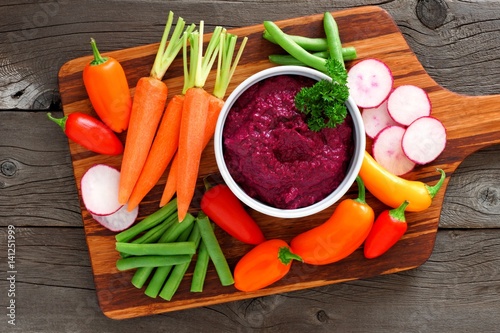 Beet hummus dip with a serving platter of fresh vegetables, above view on a wood background