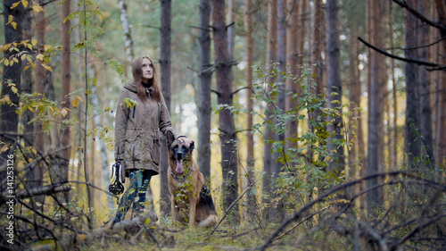 Young attractive woman and her pet - german shepherd - walking on a autumn forest