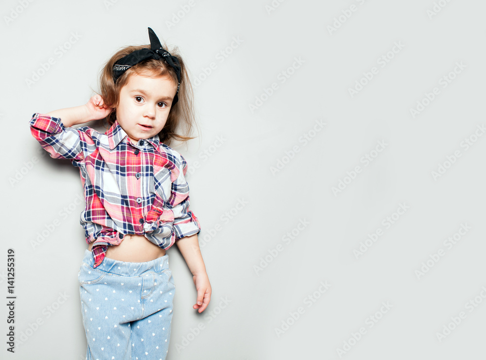 Portrait of cheerful little girl in plaid shirt and jeans standing against grey background Portrait of cheerful little girl in plaid shirt and jeans standing against grey background