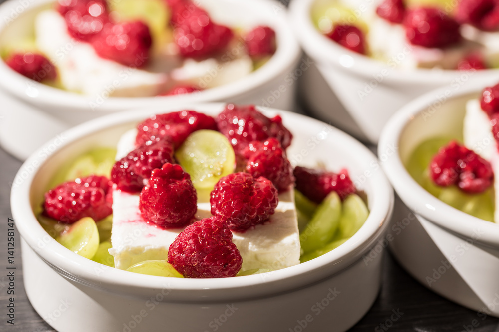White dessert bowls with cheep's cheese, green grapes and red rasperries before grilling in the oven White dessert bowls with cheep's cheese, green grapes and red rasperries before grilling in the oven