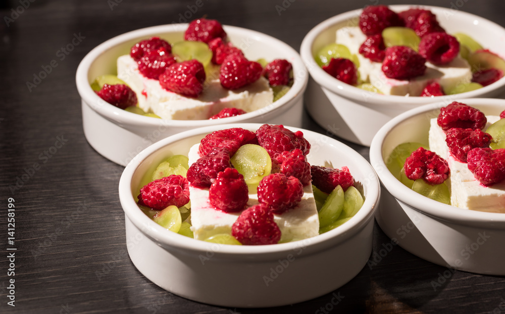 White dessert bowls with cheep's cheese, green grapes and red rasperries before grilling in the oven White dessert bowls with cheep's cheese, green grapes and red rasperries before grilling in the oven