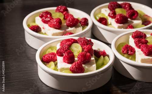 White dessert bowls with cheep's cheese, green grapes and red rasperries before grilling in the oven