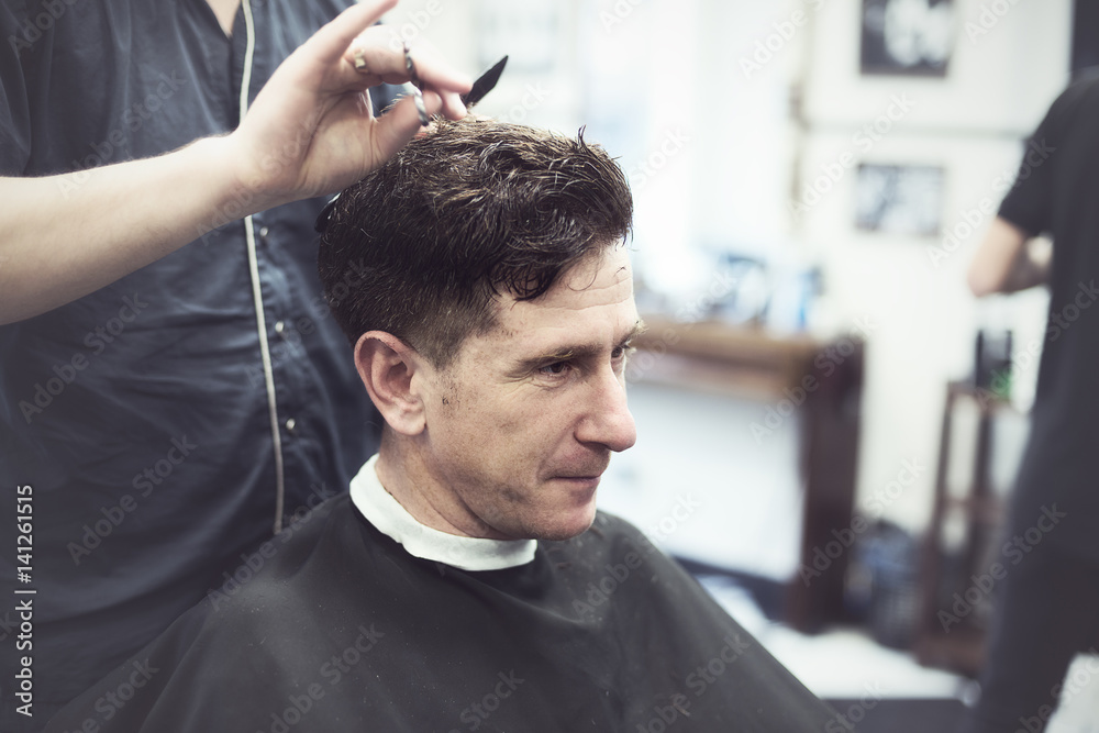 Smiling man in barbershop watching the process of hair cutting Smiling man in barbershop watching the process of hair cutting