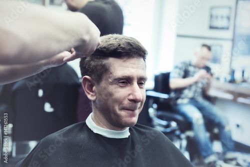 Smiling stylish man in a barbershop enjoys the process of his haircut