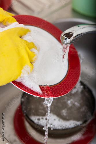 Cleaning dishware kitchen sink sponge washing dish. Close up of female hands in yellow protective rubber gloves washing photo