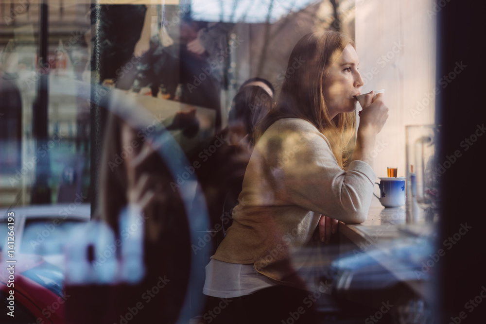 Beautiful young woman drinking coffee in coffee shop near the window