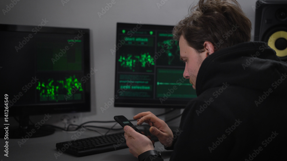 Adult male Hacker, with stubble on his face, wearing a black sports jacket sits in a secret bunker and makes cyber attacks. On your smartphone, he said the data