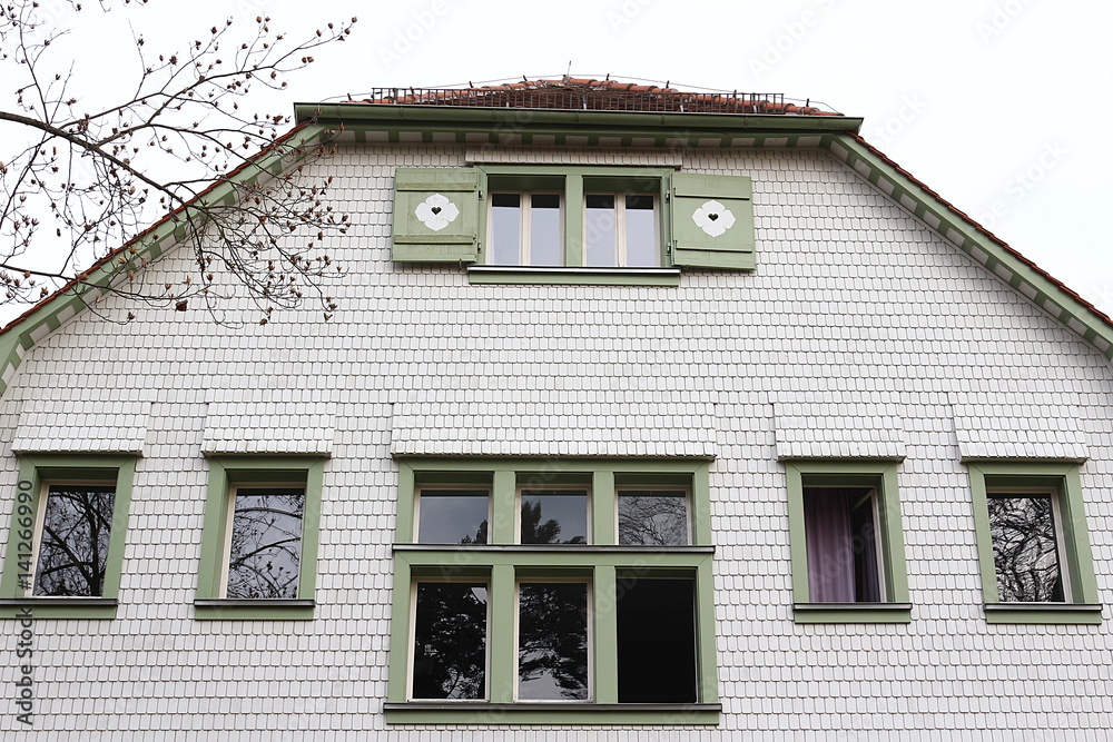 Hausfassade bedeckt mit weißen Schindel und grün eingefassten Fenstern