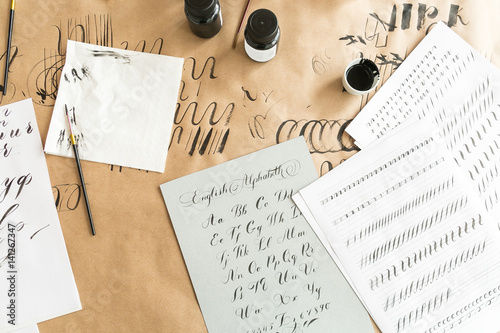 Calligraphy sheets, nibs, paper, ink and pens on a kraft background. Lettering calligraphy workshop. learning calligraphy - paper with example and brush and ink. Concept hobby. top view, flat lay.