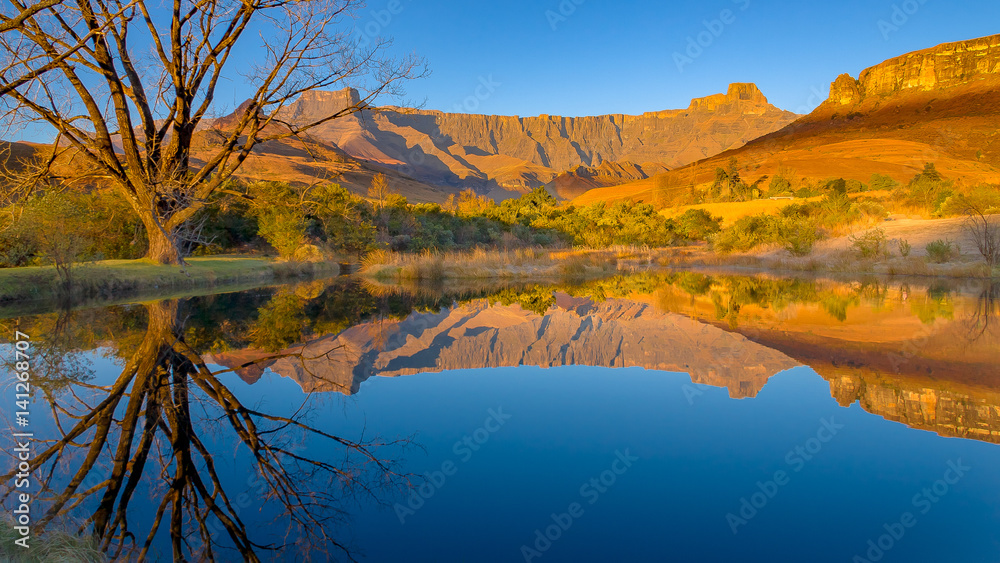 Drakensberg mountains of the amphitheatre reflected in a lake early on a mid-winter morning in South Africa Drakensberg mountains of the amphitheatre reflected in a lake early on a mid-winter morning in South Africa