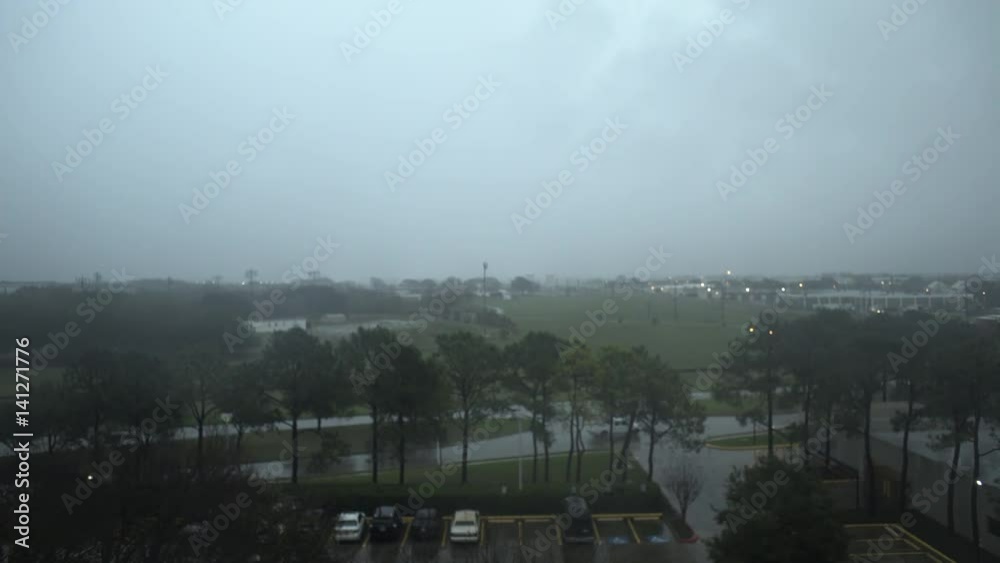 Establishing shot overlooking a parking lot and street traffic to storm clouds and rain making for very wet traveling conditions.