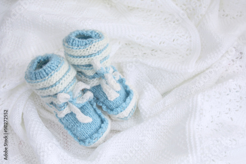 blue knitted newborn baby booties and hat on crocheted blanket white background with inscription it's a boy © Olga Lietunova
