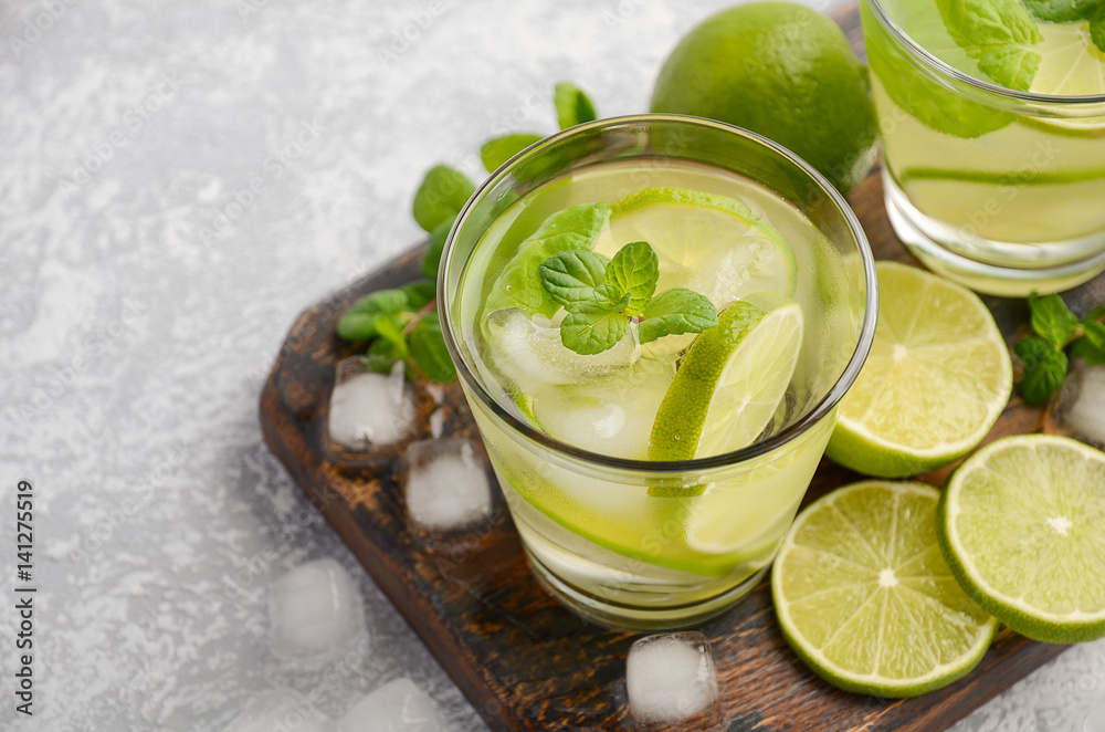 Cold refreshing summer drink with lime and mint in a glass on a grey concrete or stone background, selective focus, copy space. Cold refreshing summer drink with lime and mint in a glass on a grey concrete or stone background, selective focus, copy space.