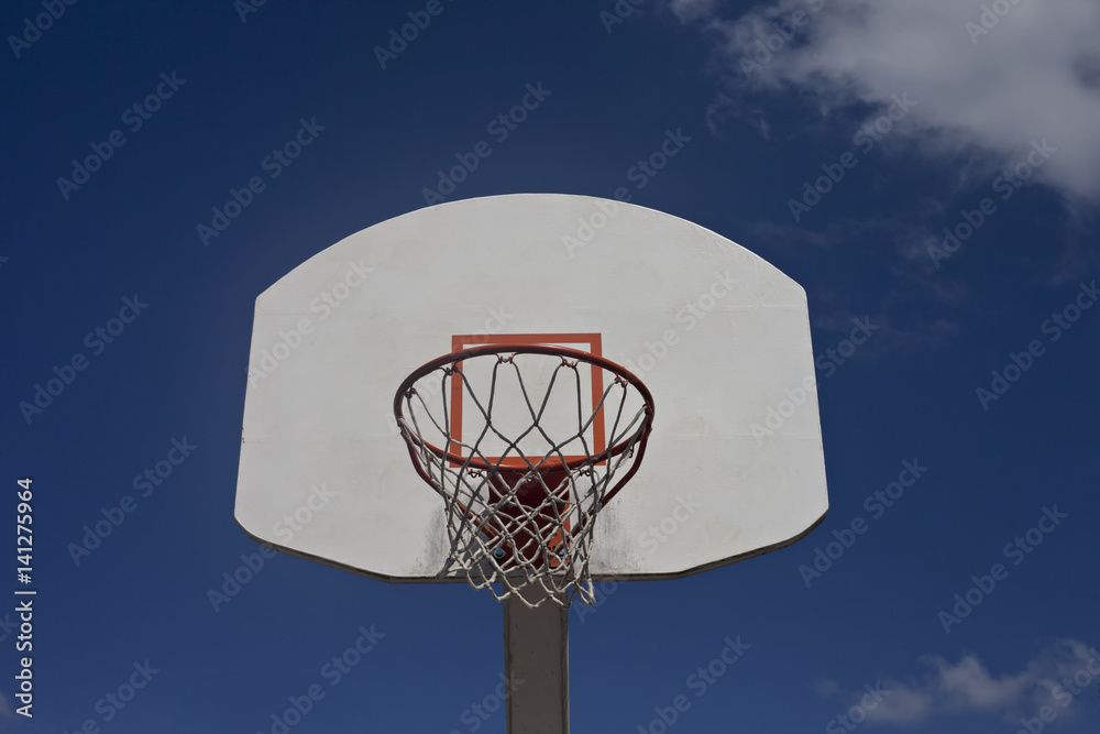 Cloudy blue sky frames old orange and white basketball goal.