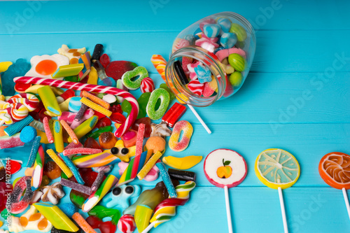 View from above on cattered candies and lollipops as fruits near glass can with chewing sweets