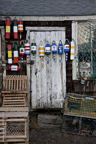 Bright, colorful bouys hanging on a rustic shed surrounded by wood lobster traps and cages.