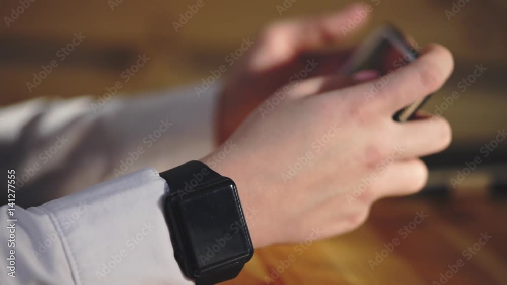 Close up shot of a businesswoman hands who put on a smart watch to quickly view the latest news. In her hands a smartphone perhaps he looks through latest news from the stock exchange of companies. Close up shot of a businesswoman hands who put on a smart watch to quickly view the latest news. In her hands a smartphone perhaps he looks through latest news from the stock exchange of companies.