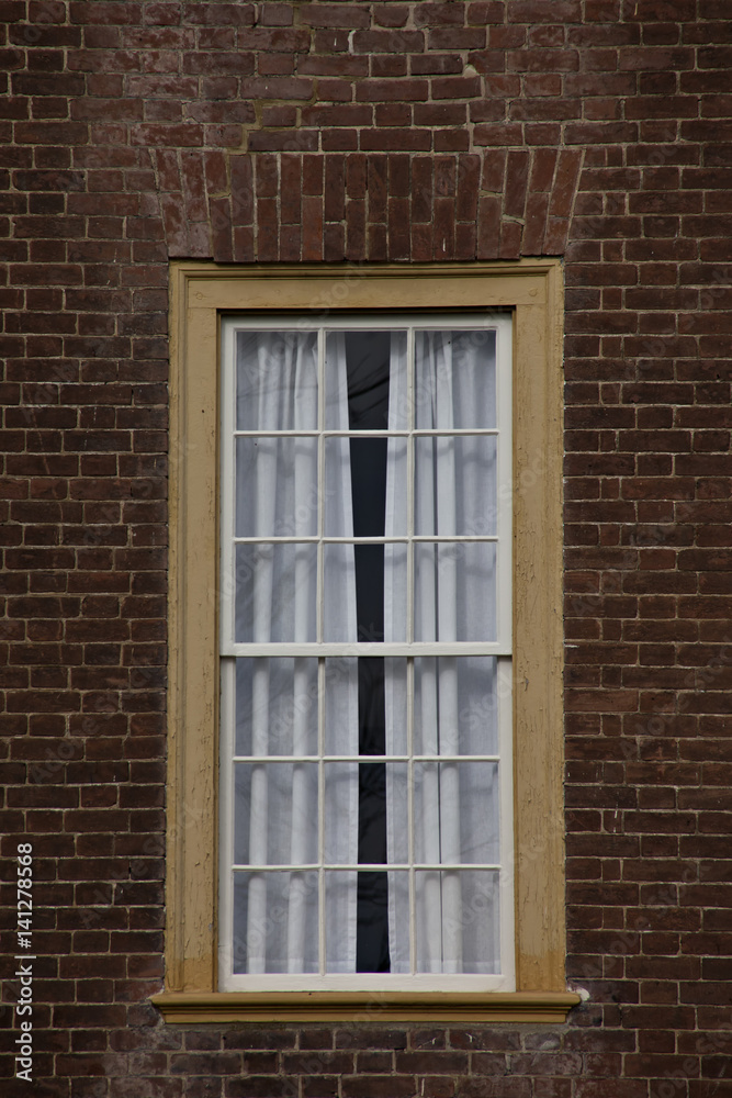 Fototapeta premium Single yellow framed window on red brick wall.