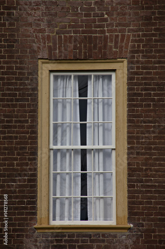 Single yellow framed window on red brick wall.
