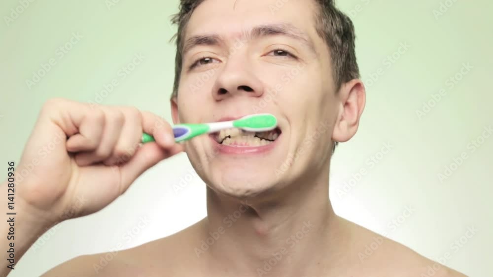 Young smiling man brushing teeth with toothbrush on isolated light background Young smiling man brushing teeth with toothbrush on isolated light background