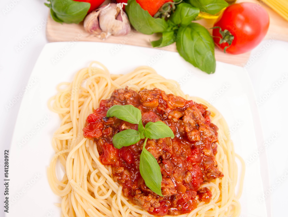 Spaghetti bolognese,some tomatoes, olive oil, basil, garlic, and raw pasta in the background Spaghetti bolognese,some tomatoes, olive oil, basil, garlic, and raw pasta in the background