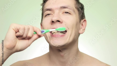 Wallpaper Mural Young smiling man brushing teeth with toothbrush on isolated light background Torontodigital.ca