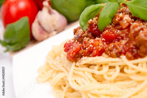 Spaghetti bolognese,some tomatoes, olive oil, basil, garlic, and raw pasta in the background