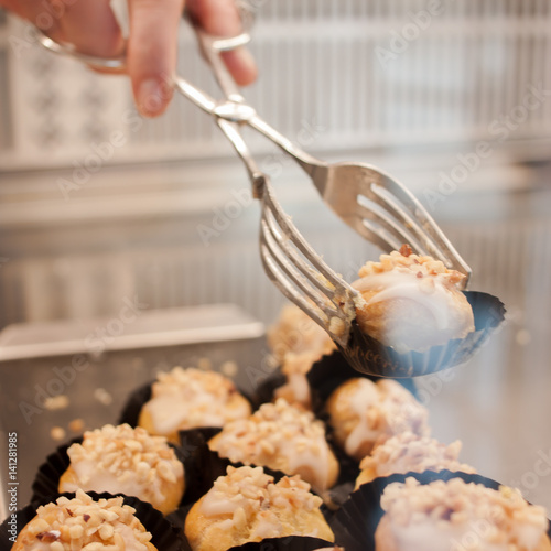 A female hand holds a tongs for a sweet little cake with cream and nuts photo