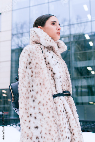 Beautiful business woman in a fur coat on a background of office on the street