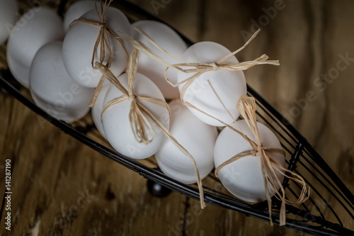 White eggs tied with a straw in a basket on a wooden background.