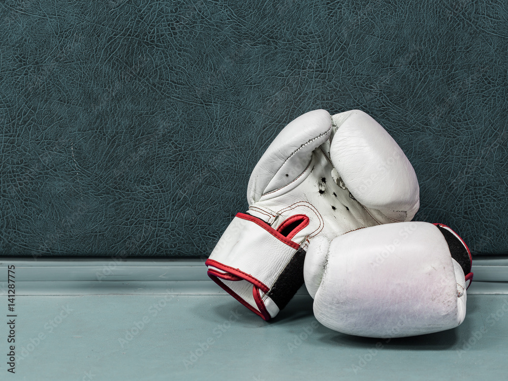 a pair of white leather boxing gloves lying on the floor near a wall