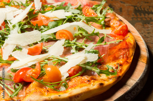 Pizza with ham, tomatoes, parmesan and arugula