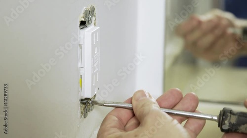 An electrician or homeowner handyman type completing the installation of a new ground fault outlet photo