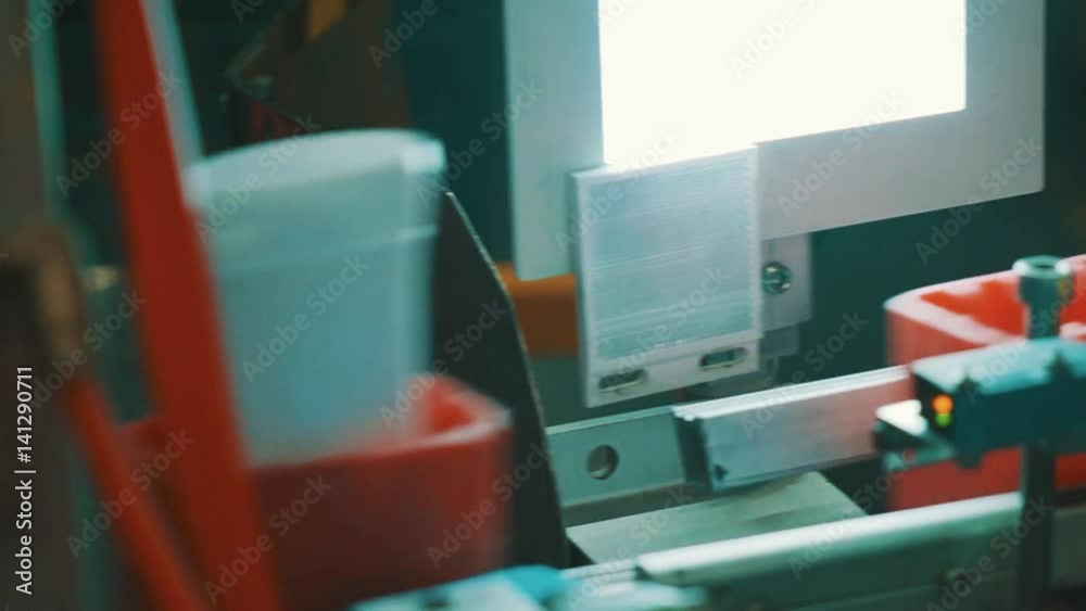 White plastic tubes in red containers moving fast on conveyor belt in front of control bright light, close up White plastic tubes in red containers moving fast on conveyor belt in front of control bright light, close up
