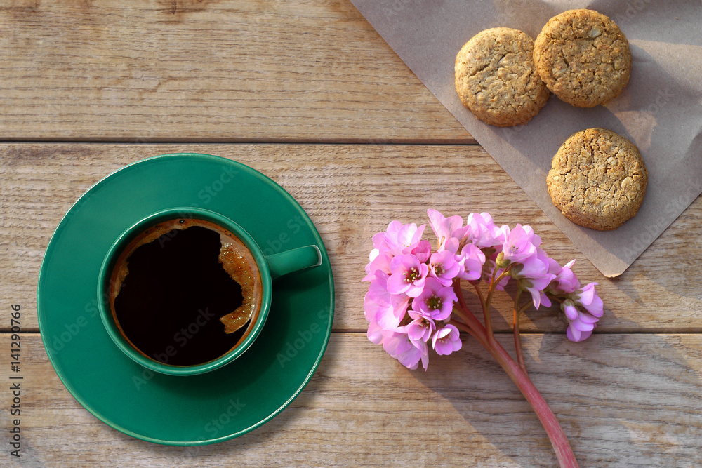 Arrangement of a coffee in a green cup with biscuits on a table with a spring blossoms-top view

