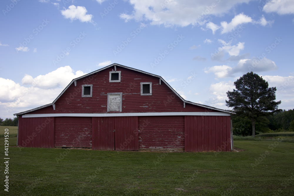 Large, beautiful red barn on bright green grass, surrounded by cloudy blue sky Large, beautiful red barn on bright green grass, surrounded by cloudy blue sky
