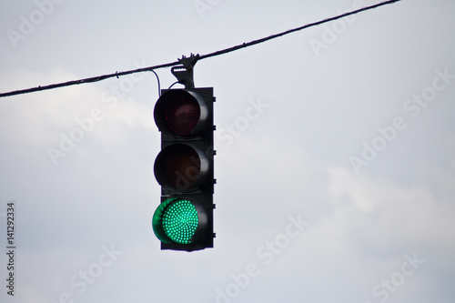 Green traffic light surrounded by overcast sky.