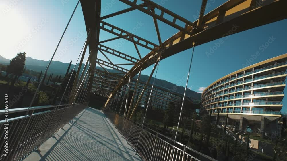 Bridge over road to modern elite resort under blue sky in front of mountains on hot summer sunny day, tracking shot Bridge over road to modern elite resort under blue sky in front of mountains on hot summer sunny day, tracking shot