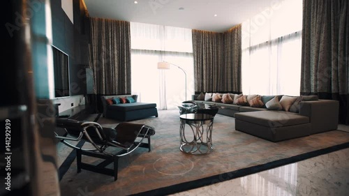 Expensive living room interior, long sofa big TV screen, bright light outside panoramic windows with curtains